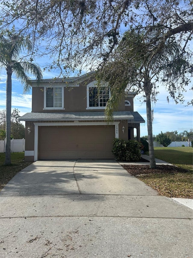 traditional-style home featuring an attached garage, driveway, fence, and stucco siding