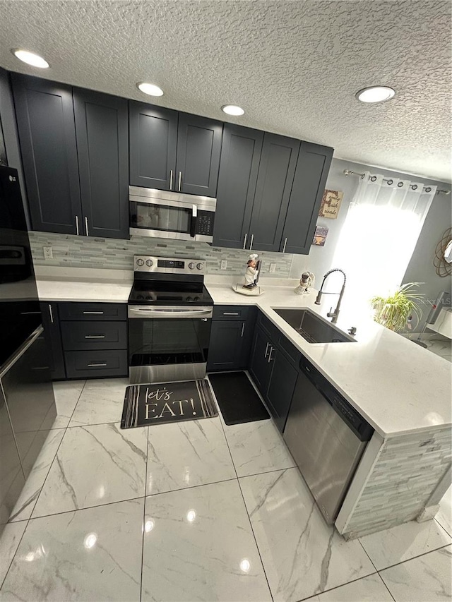 kitchen featuring a sink, marble finish floor, appliances with stainless steel finishes, light countertops, and decorative backsplash