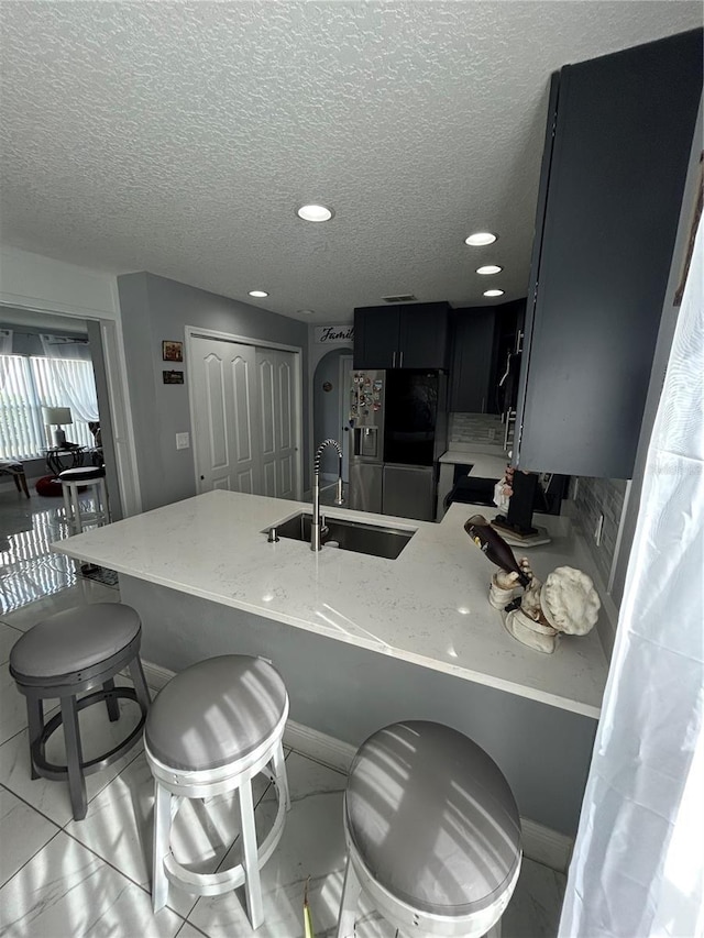 kitchen featuring light stone counters, a breakfast bar, a peninsula, refrigerator with ice dispenser, and a sink