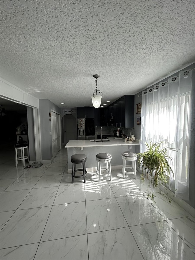 kitchen featuring arched walkways, light countertops, fridge with ice dispenser, a sink, and dark cabinets