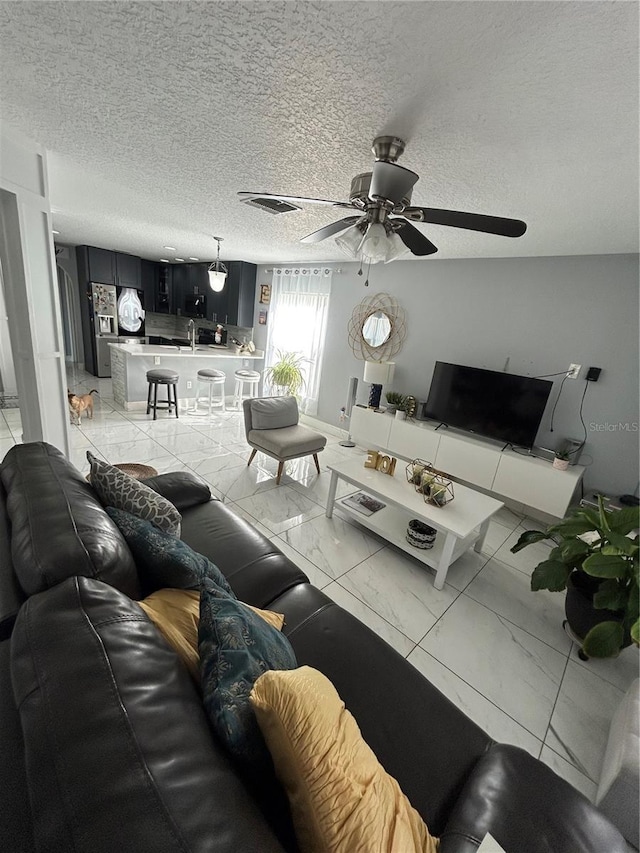 living room with a textured ceiling, marble finish floor, ceiling fan, and visible vents