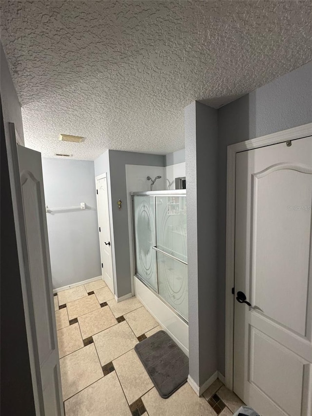 bathroom featuring baseboards, enclosed tub / shower combo, visible vents, and a textured ceiling