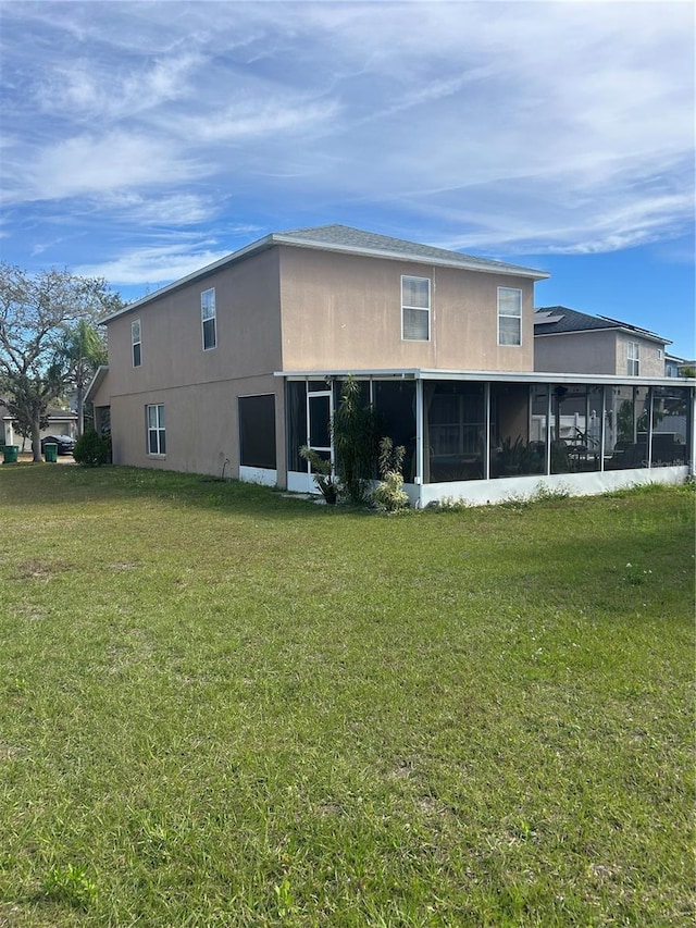 back of house featuring a sunroom, a lawn, and stucco siding