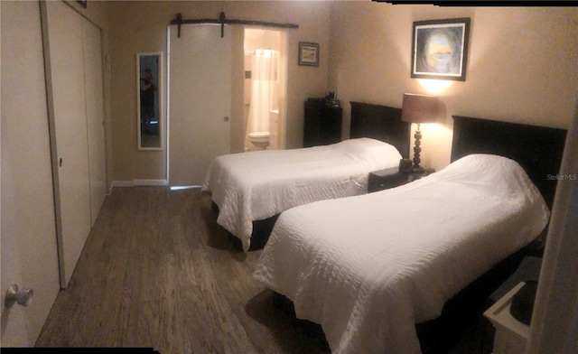 bedroom featuring wood finished floors, ensuite bath, and a barn door