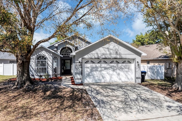 ranch-style home featuring concrete driveway, an attached garage, fence, and stucco siding