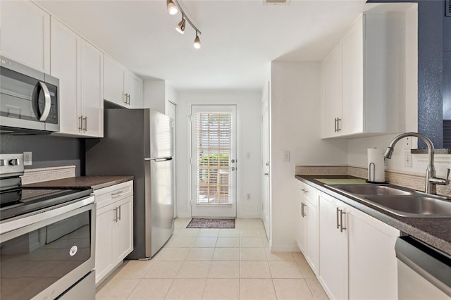 kitchen with stainless steel appliances, dark countertops, white cabinets, and a sink