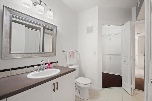 bathroom featuring tile patterned flooring, toilet, vanity, visible vents, and a walk in closet