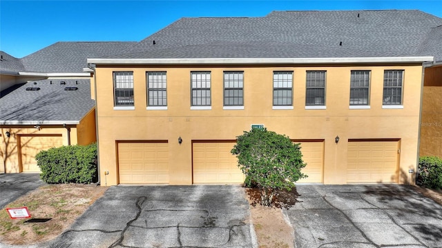 multi unit property featuring driveway, an attached garage, roof with shingles, and stucco siding