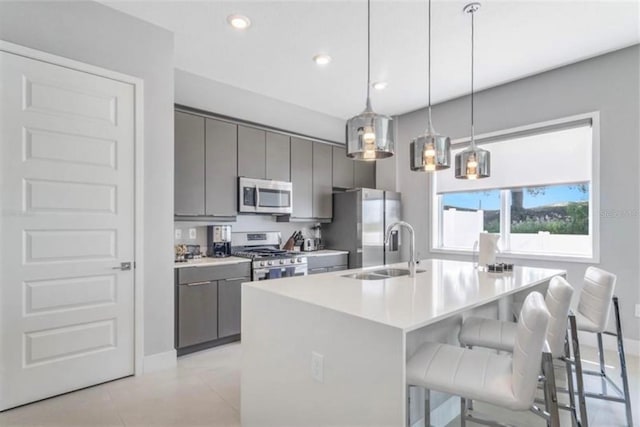 kitchen featuring a sink, gray cabinetry, a kitchen bar, appliances with stainless steel finishes, and a kitchen island with sink