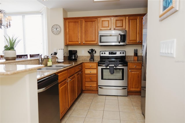 kitchen with light tile patterned floors, brown cabinetry, a peninsula, a sink, and stainless steel appliances