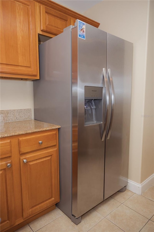 kitchen featuring light stone counters, light tile patterned floors, stainless steel refrigerator with ice dispenser, and brown cabinets