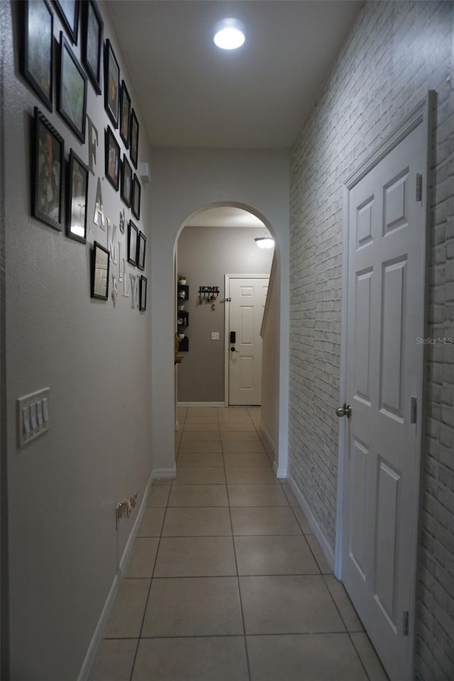 hallway with light tile patterned floors, brick wall, arched walkways, and baseboards