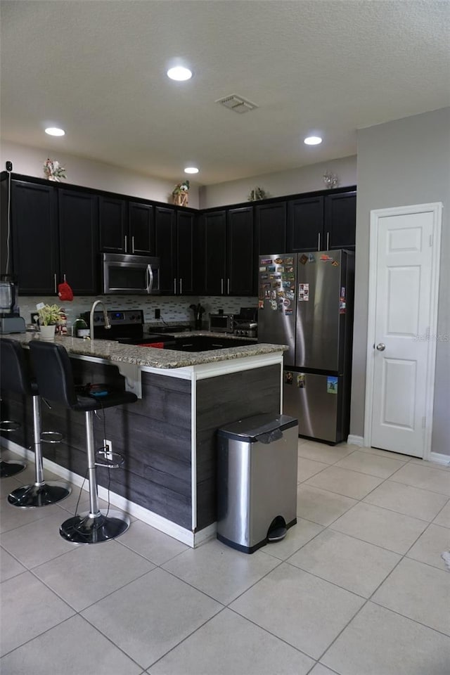 kitchen with stainless steel appliances, light stone countertops, dark cabinets, and light tile patterned floors