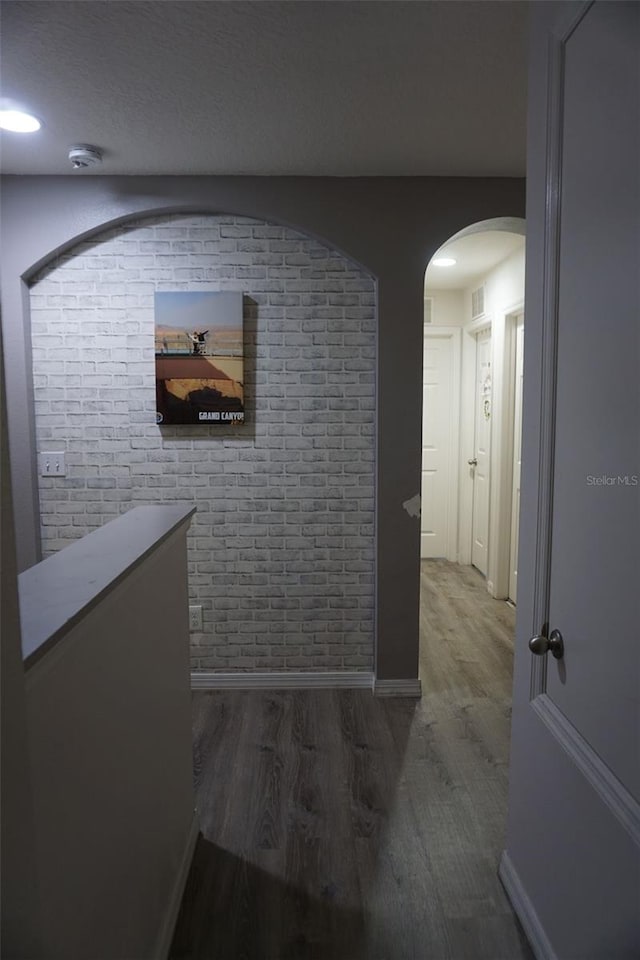 hall featuring baseboards, arched walkways, brick wall, wood finished floors, and a textured ceiling