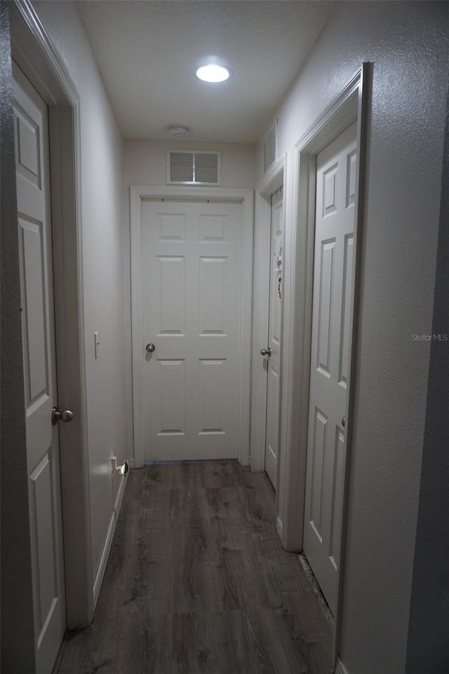 corridor featuring dark wood-style floors, visible vents, and baseboards