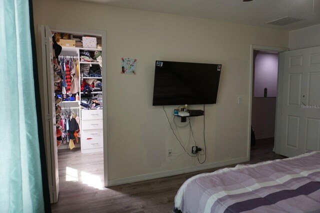 bedroom featuring wood finished floors, a closet, a walk in closet, and baseboards