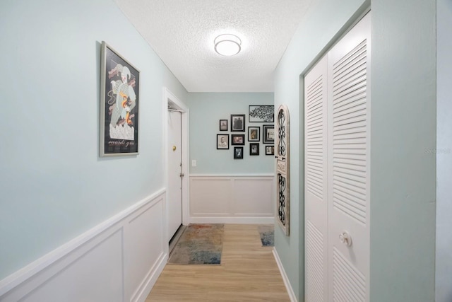 hallway with light wood-style flooring, a wainscoted wall, a decorative wall, and a textured ceiling