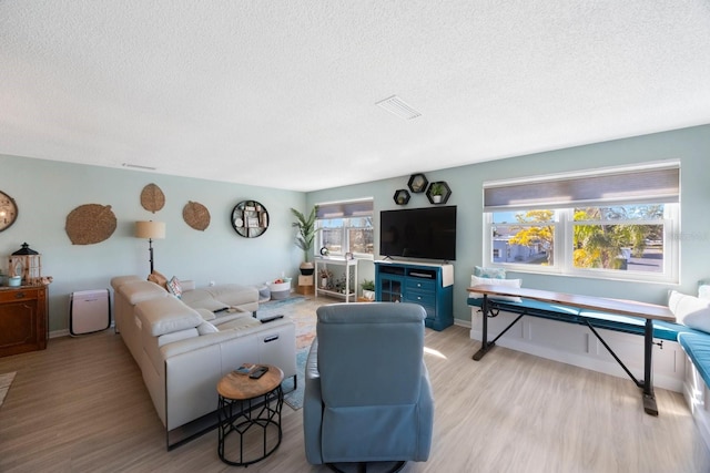 living room featuring light wood finished floors, baseboards, visible vents, and a textured ceiling