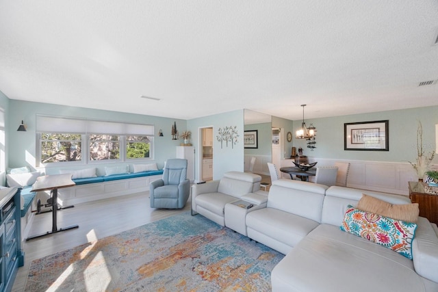 living area with wood finished floors, visible vents, a textured ceiling, and an inviting chandelier