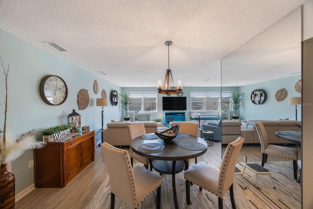 dining space with a notable chandelier, visible vents, a textured ceiling, light wood-type flooring, and baseboards