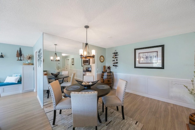 dining area featuring a chandelier, a wainscoted wall, a textured ceiling, and wood finished floors