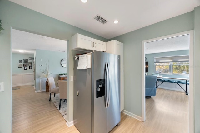 kitchen featuring stainless steel refrigerator with ice dispenser, light wood finished floors, visible vents, white cabinets, and baseboards