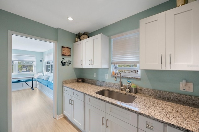 kitchen with white cabinetry, a sink, and light stone countertops