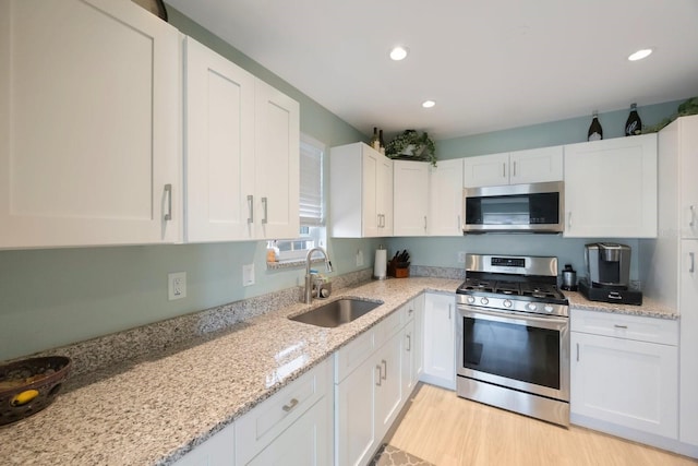 kitchen with appliances with stainless steel finishes, light stone countertops, light wood-style floors, white cabinetry, and a sink