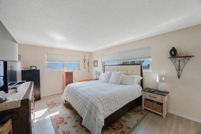 bedroom with baseboards, a textured ceiling, and light wood finished floors