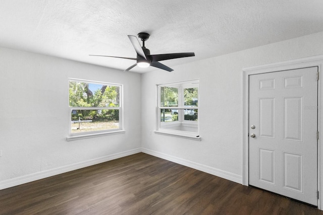 unfurnished room featuring a wealth of natural light, a textured ceiling, baseboards, and dark wood-type flooring