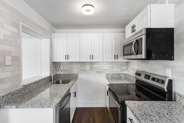 kitchen featuring dark wood finished floors, light stone countertops, stainless steel appliances, white cabinetry, and a sink