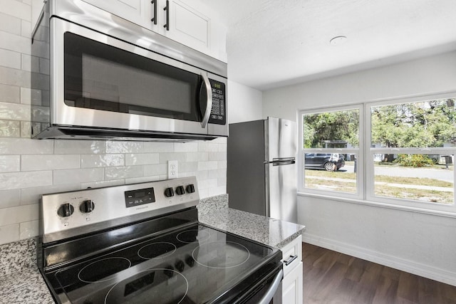 kitchen with dark wood-style flooring, stainless steel appliances, tasteful backsplash, light stone countertops, and baseboards