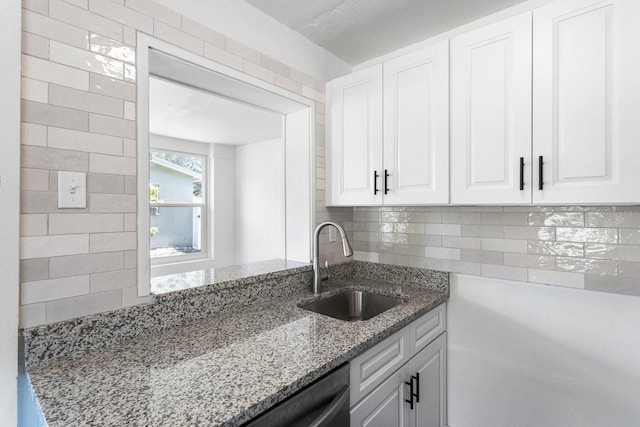 kitchen with light stone countertops, tasteful backsplash, white cabinets, and a sink