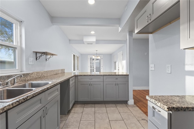 kitchen with light tile patterned floors, a peninsula, gray cabinetry, a sink, and a notable chandelier