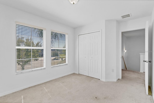 unfurnished bedroom featuring baseboards, visible vents, a closet, and light colored carpet