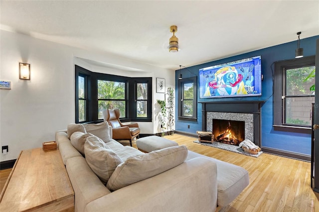 living room with a warm lit fireplace, baseboards, and wood finished floors