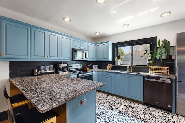 kitchen with a breakfast bar area, blue cabinetry, stainless steel appliances, a sink, and a peninsula