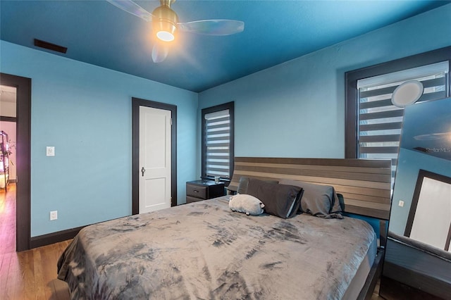 bedroom with a ceiling fan, visible vents, baseboards, and wood finished floors