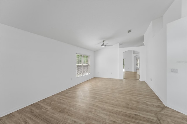 empty room with light wood-style floors, arched walkways, visible vents, and a ceiling fan