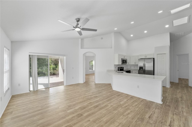 kitchen with arched walkways, light wood-style flooring, stainless steel appliances, a peninsula, and light countertops