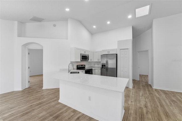 kitchen with arched walkways, appliances with stainless steel finishes, a sink, high vaulted ceiling, and a peninsula