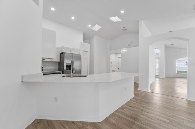 kitchen with light countertops, arched walkways, stainless steel fridge, and light wood finished floors