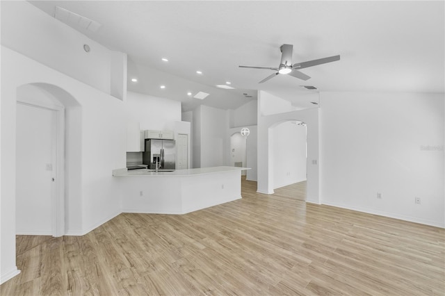 unfurnished living room featuring light wood-style floors, arched walkways, ceiling fan, and lofted ceiling