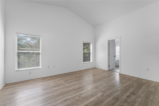 spare room with high vaulted ceiling, light wood-style flooring, and baseboards