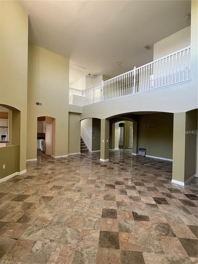 unfurnished living room featuring visible vents, stone finish flooring, stairway, arched walkways, and baseboards