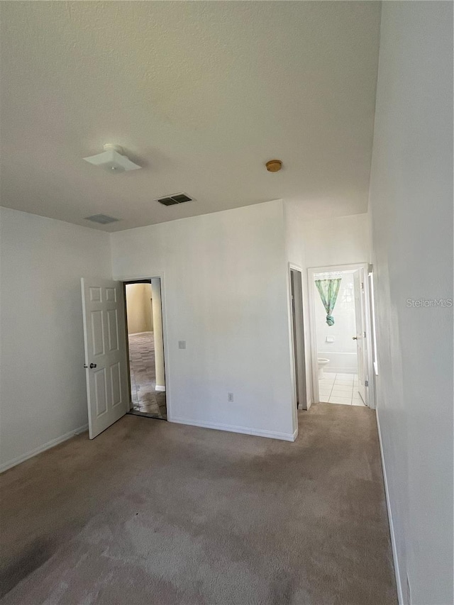 empty room featuring visible vents, carpet floors, a textured ceiling, and baseboards