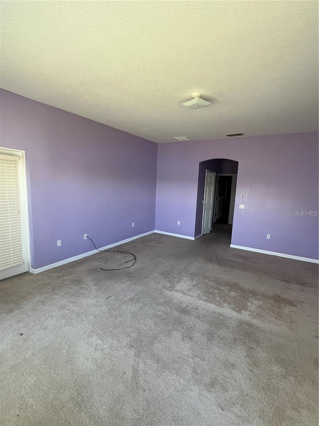 carpeted empty room featuring arched walkways, a textured ceiling, and baseboards