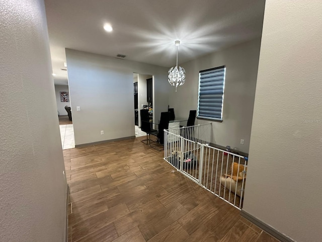 hall featuring a notable chandelier, wood tiled floor, visible vents, and baseboards