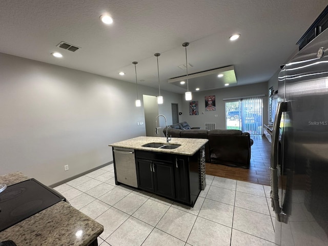 kitchen featuring visible vents, appliances with stainless steel finishes, open floor plan, a sink, and dark cabinets