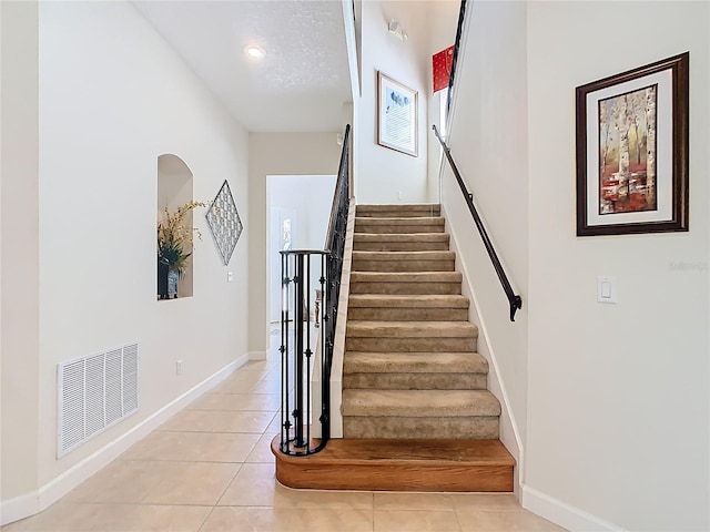 stairway featuring baseboards, visible vents, and tile patterned floors